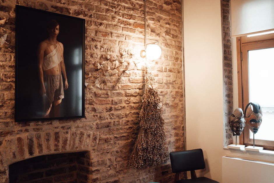 Interior of light cafe with brick wall decorated with picture of man near lamp and hanging garland with dry herbs near chair and window with African masks on windowsill